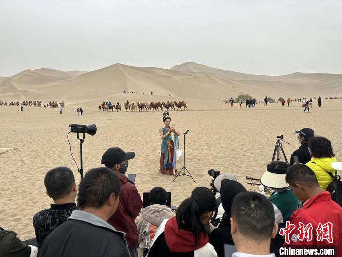 圖為2023年4月底，敦煌大漠“逐舞者”奧楠在鳴沙山月牙泉景區(qū)視頻直播，吸引游人圍觀。　馮志軍 攝